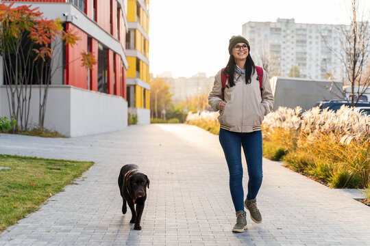Caucasian gorgeous woman looking away while walking with her dog through the street and enjoying a good sunny weather. Walking and taking care of the pet concept