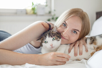 Young 30s happy woman with a cat lying in bed at home. Stay home stay safe. Love, care, adoption
