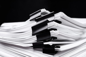 A stack of office papers, some of which are fastened with black binders