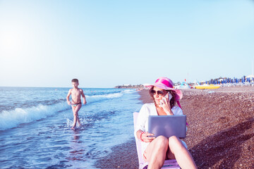 woman smart working on the beach with phone and laptop.