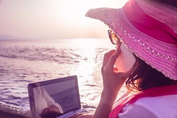 woman smart working on the beach with phone and laptop seen from behind