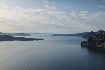 Breathtaking view of Fira, Oia, the volcano and a small boat leaving the port of Athinios in Santorini Greece