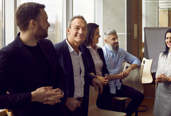 Portrait of senior businessman standing surrounded by his colleagues who are talking in coworking...