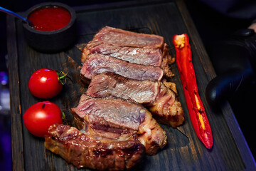 The waiter holds a dish with steak with sauce, tomatoes and red hot peppers