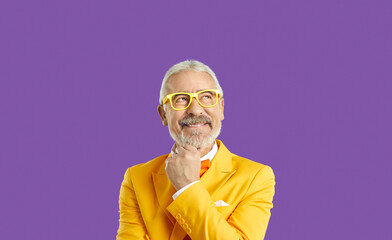 Dreamy delighted elderly man look up empty space, stand in contemplation thinking, isolated on purple color studio background. Handsome wealthy caucasian male in stylish yellow suit. Business people