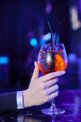 A girl in a nightclub holds a glass with an alcoholic cocktail in her hand