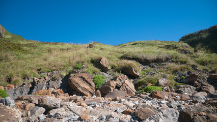 Fototapeta na wymiar Acantilado rocoso cubierto de hierba verde y cielo azul