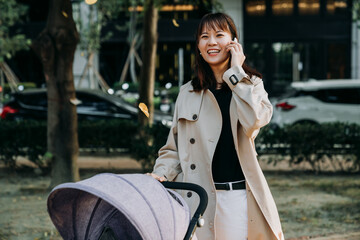 portrait cheerful asian trendy mother is having a pleasant phone talk while taking a stroll with a...