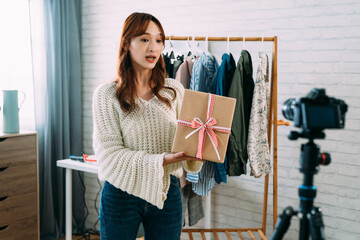 selective focus asian ecommerce business owner selling clothing is presenting a wrapped gift box in...