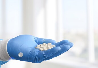 A medical worker or pharmacist hands wearing blue latex protective gloves, pouring white medicine pills