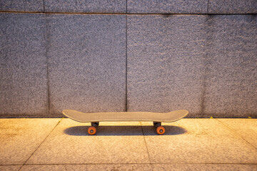 Skateboard and illuminated gray wall in city
