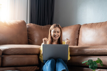 Young Asian woman celebrate success or happy pose with laptop at living home.