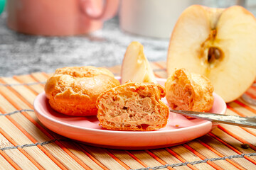 Pink saucer with eclairs and apple slices on the kitchen table. Photo of food.