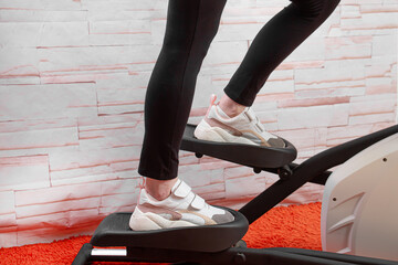 A middle-aged woman goes in for sports on an elliptical trainer at home.