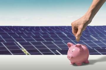 Unrecognizable manager putting coin into piggy bank while saving money near photovoltaic panel on...