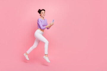 Fototapeta na wymiar Full length body size view of lovely cheery trendy girl jumping using device copy space isolated over pink pastel color background