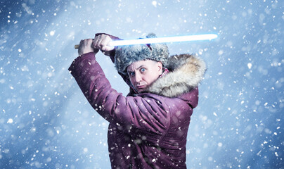 Man in winter clothes with a wooden lightsaber in his hands on a blue background with falling snow.