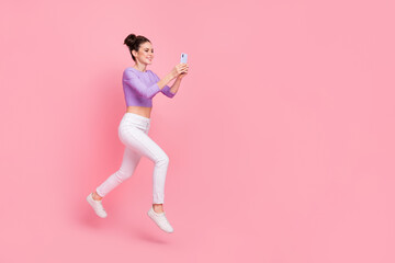Fototapeta na wymiar Full length body size view of lovely trendy girl jumping using gadget copy space isolated over pink pastel color background