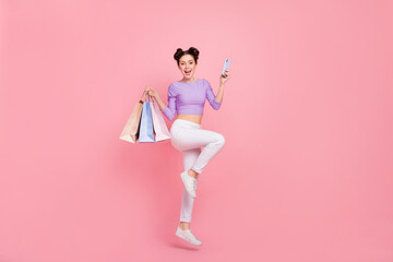 Full length body size view of pretty trendy girl jumping using device buy clothes wear isolated over pink pastel color background