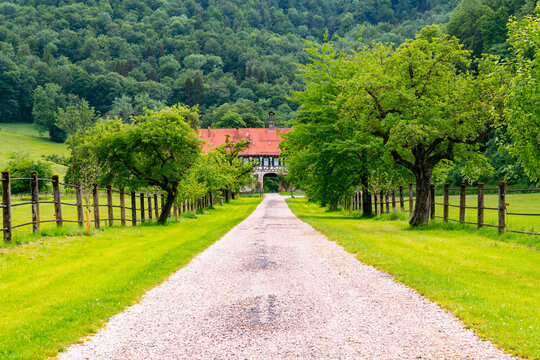 Access to historic monastery farmhouse with picturesque alley way and half timbered facade. Tourist attraction near “Uracher Wasserfall“ cascade in rural landscape in Germany with pasture and meadows.