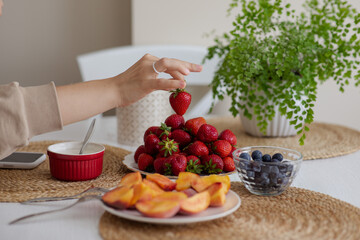 The girl holds a krubnik in her hand and is going to eat it. A healthy fruit breakfast. Abundance of summer berries. Kubnik and blueberry