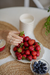 The girl holds a krubnik in her hand and is going to eat it. A healthy fruit breakfast. Abundance of summer berries. Kubnik and blueberry