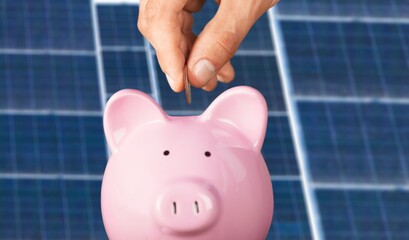 Unrecognizable manager putting coin into piggy bank while saving money near photovoltaic panel on...