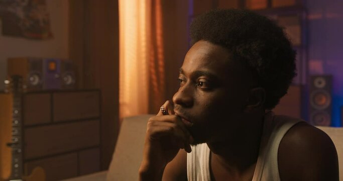 Lonely guy sits in living room on couch, man stares at window thoughtful, sad, longing, hurt, experiencing negative emotions after breakup with girlfriend.
