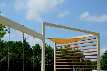 yellow canvas stretched, shading from the sun and rain over the terrace of the restaurant, on the playground in the kindergarten, on promenade. pergola with wooden gray beams, on white metal steel