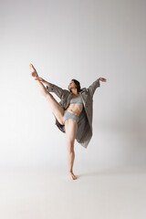 Fototapeta premium Happy young beautiful woman in lingerie and coat moves isolated on grey background. Dance, beauty, action, flexibility, inspiration concept.