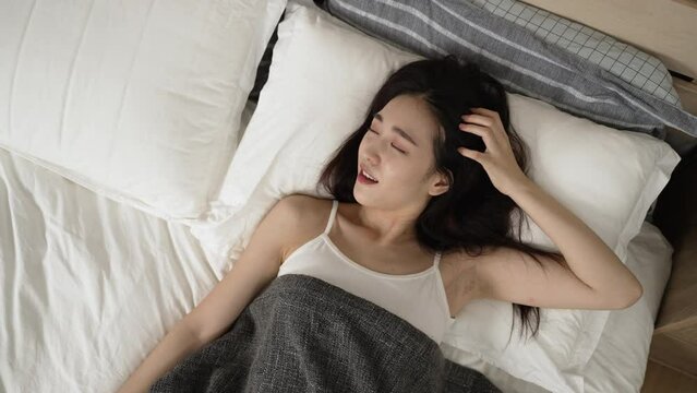top angle of beautiful asian woman just waking up on bed is touching hair and smiling with happiness while enjoying the tranquil morning in the bedroom at home