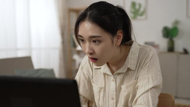 asian woman employee working from home is looking at computer in surprise and rejoicing over job promotion online notification while replying message