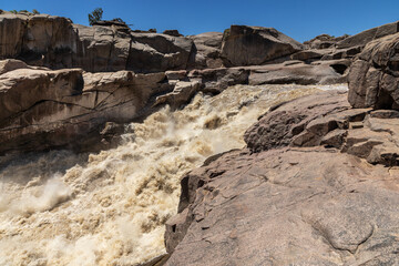 Rapid flowing flood waters of the Orange river at Augrabies waterfall in the Northern Cape Province of South Africa. Around is granite rock formations. 