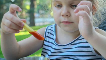 Little girl eat french fries. Close-up of blonde girl takes potato chips with her hands and tries...