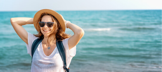 Portrait of a young cheerful woman in a sunglasses hat with a backpack on the background of the blue sea