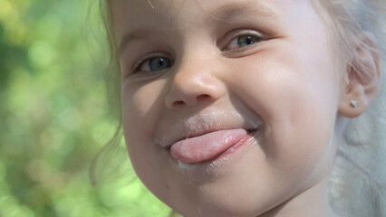Portrait of cute little girl sticking her tongue out and smiling after eating delicious ice cream. Extreme close-up portrait of little girl.