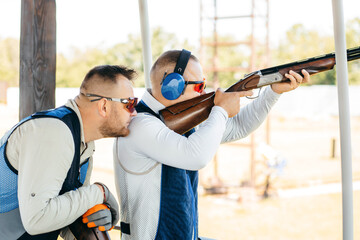 Two adult mans in sunglasses and a rifle vest practicing fire weapon shooting. Two young...