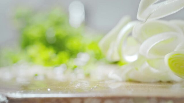Rings of Sliced Leek Thrown onto a Wet Wooden Chopping Board Rolling and Splashing Droplets in Slow Motion