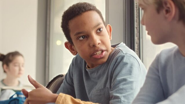 Chest up slowmo of African American middle school boy talking to classmate while having break at school corridor