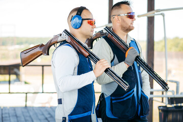 Portraits of two adult mans in sunglasses, protective headphones and a rifle vest practicing fire...