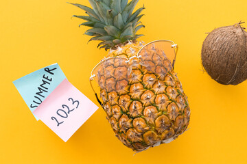 Funny pineapple with sunglasses and word summer 2023 on yellow background