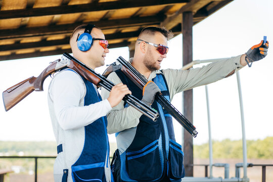 Two adult mans in sunglasses and a rifle vest practicing fire weapon shooting. Two young experienced shooters aiming shotgun in outdoor.