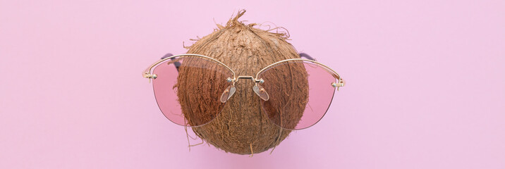 Fresh coconut wearing sunglasses on a bright pink background. Hello summer