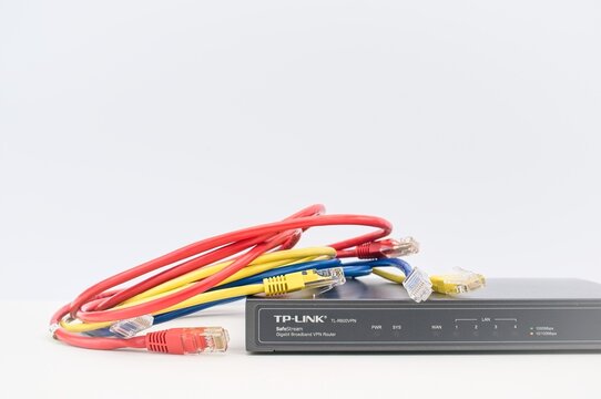 TP-LINK broadband network router with RG45 cables on a desk with white wall background