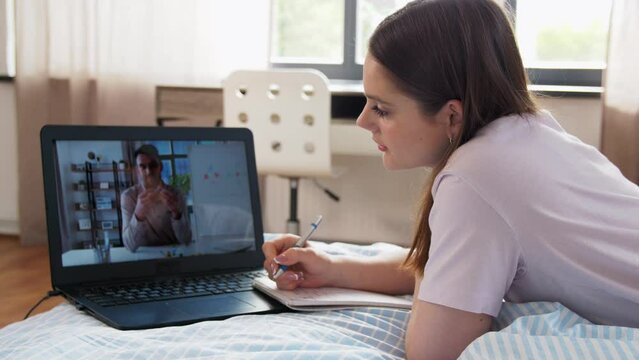school, online education and e-learning concept - teenage student girl with laptop computer having chemistry class and writing to notebook lying on bed at home