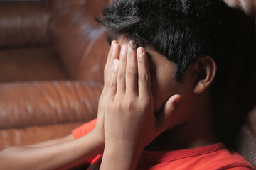 sad teenage boy covering his face sitting on sofa 