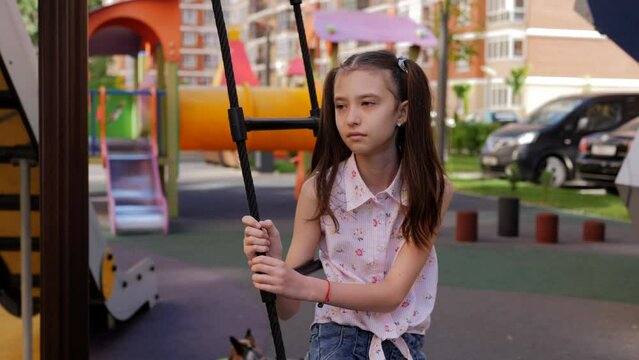 A sad lonely girl is slowly swinging on a swing in the playground.
