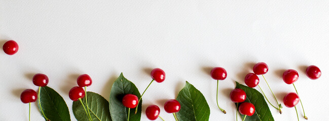 Long narrow banner. Summer theme. Juicy red cherries with leaves on a white background.