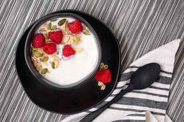 Overhead view of vanilla yogurt with granola and fresh raspberries; copy space