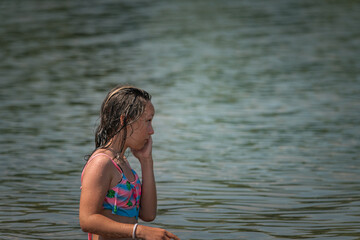 A little girl splashes in a pond during the day.